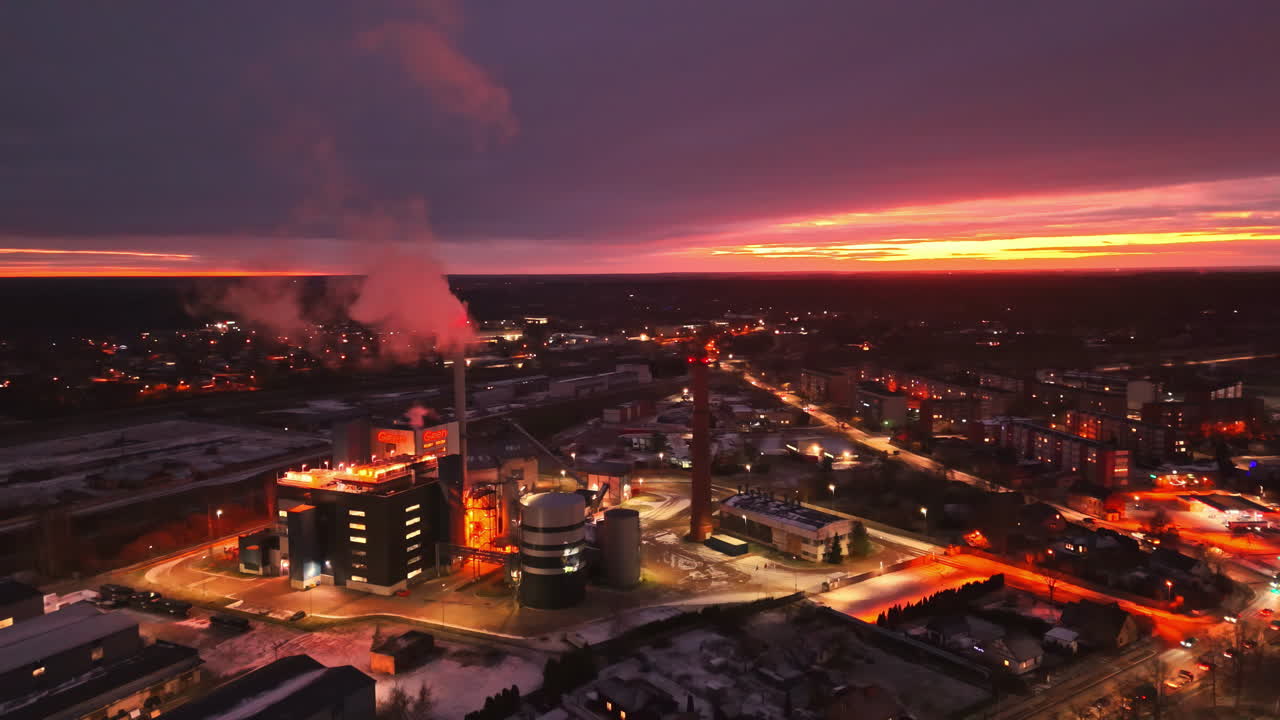Evening aerial of energy facility at sunset with glowing smoke stack and lights