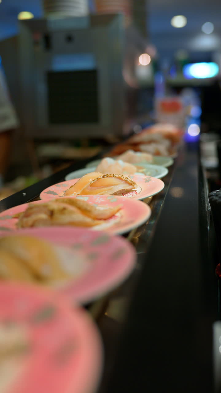 Close up of plates with sushi placed on a rotating conveyor belt moving through the restaurant. Vertical