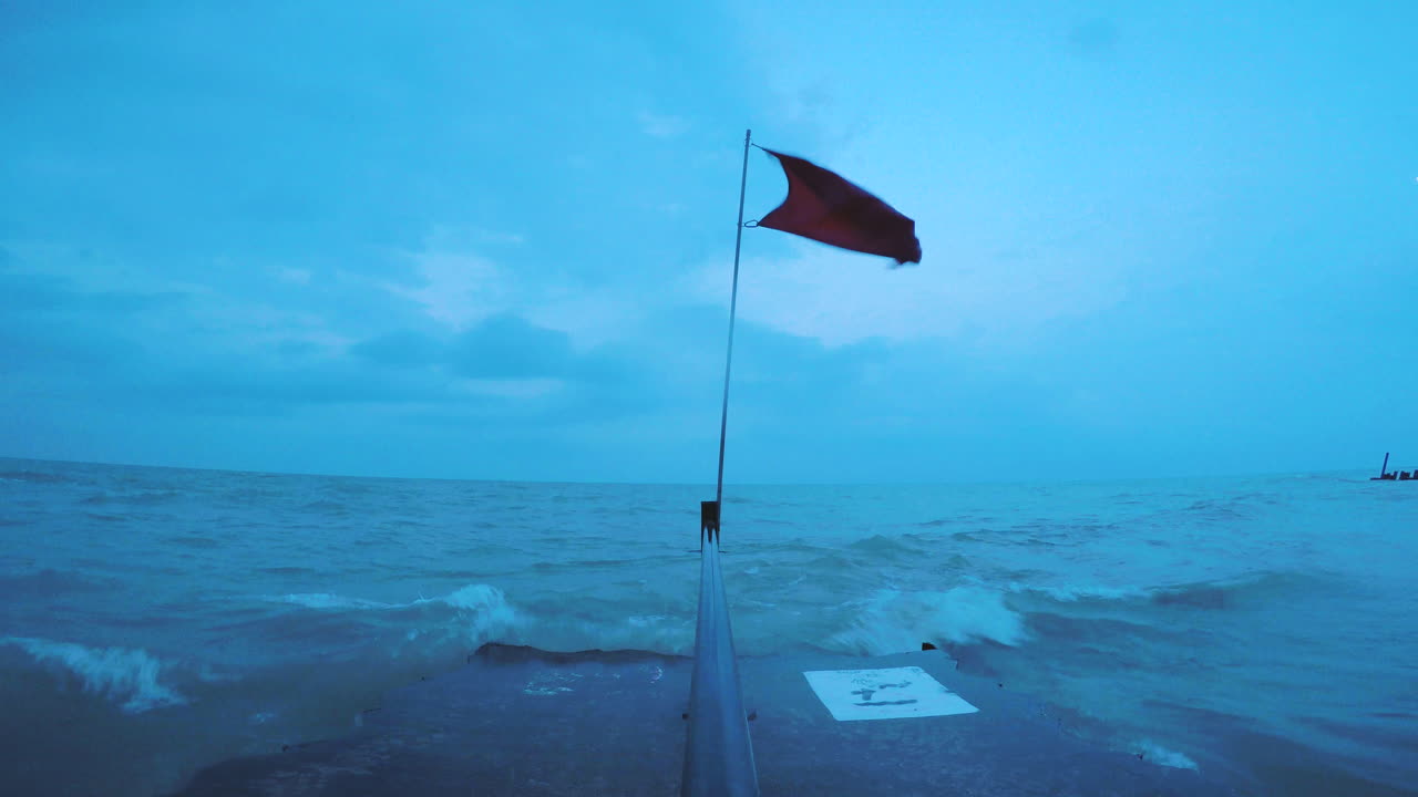 la bandera roja rota ondea agresivamente en el viento mientras fuertes olas a orillas del lago chocan contra el muelle