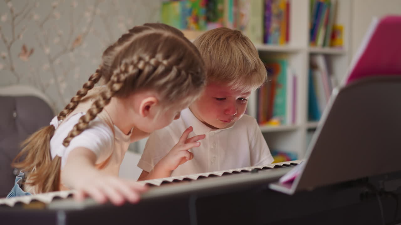 Little girl with plaits amuses crying brother at piano