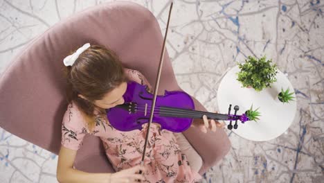 young girl sitting on sofa in living room playing violin. musicianship.