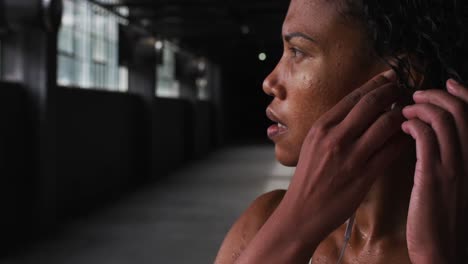 Portrait-of-african-american-woman-standing-in-an-empty-building-putting-earphones-in