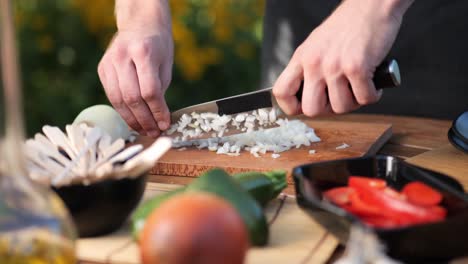 Young-man-chops-onions-on-a-wooden-board-in-his-garden-close-up