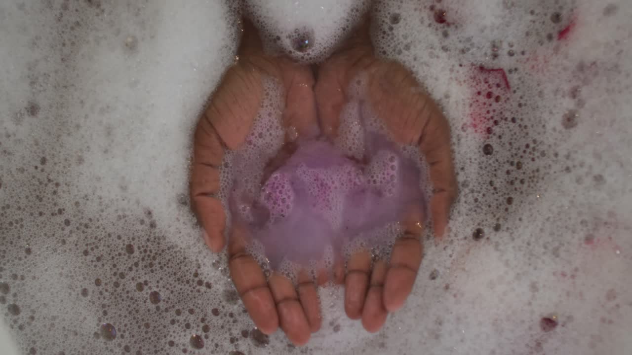 Hands of african american attractive woman taking bath with foam, salt and rose petals