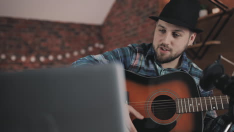 joven músico masculino transmitiendo un video tutorial, tocando la guitarra en casa 1