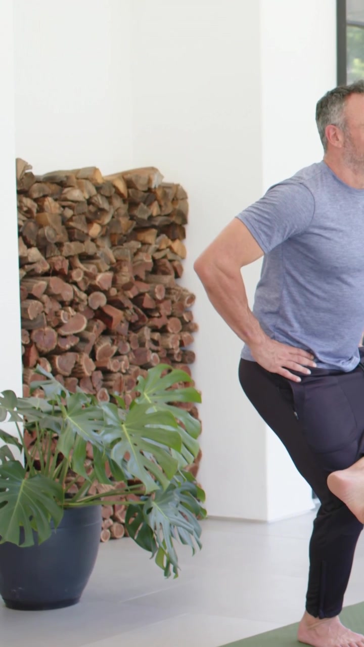 Panning pair in black, blue shirts moving to single-leg balance on green mat during home workout