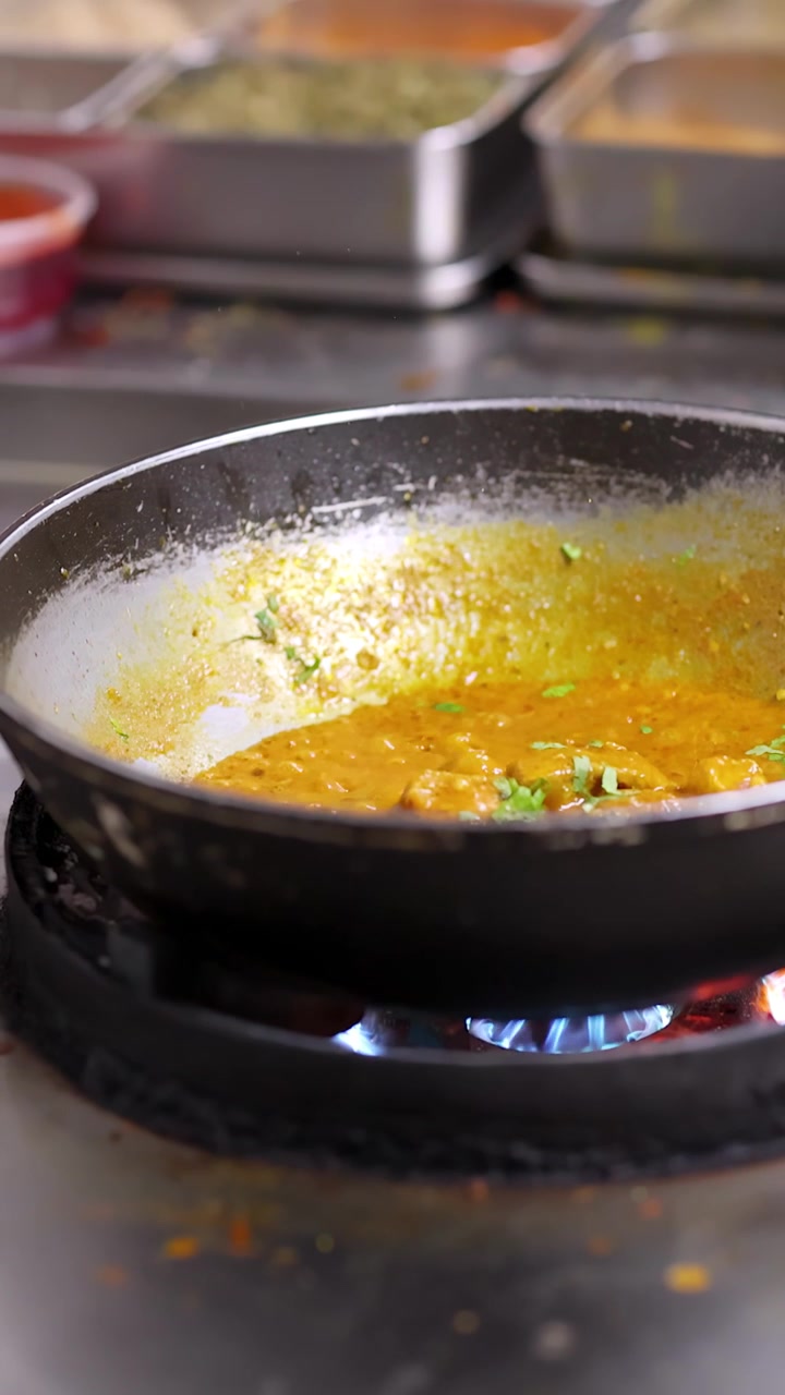 Primo piano di curry giallo che sobbolle in una padella su un fornello a gas con fiamma blu