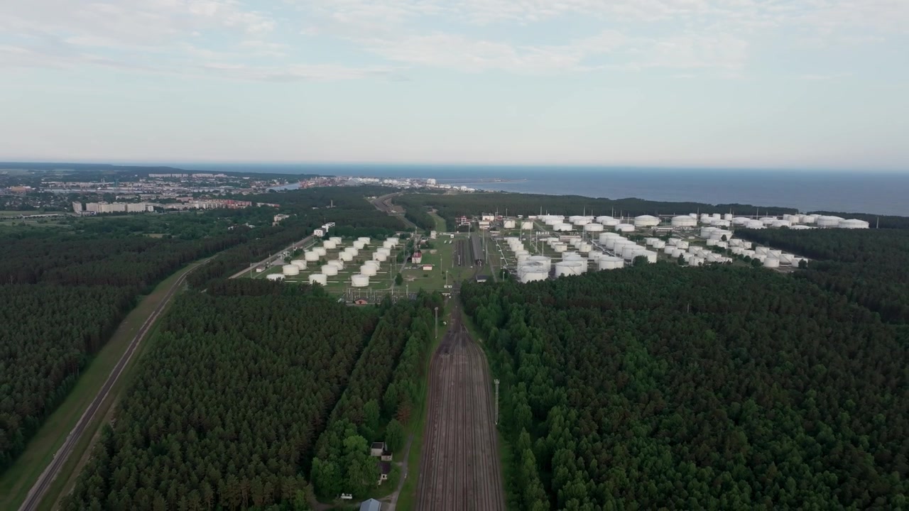 Riprese aeree con drone che mostrano un grande terminal di stoccaggio petrolifero con infrastrutture ferroviarie circondato da foreste vicino alla costa del Mar Baltico a Ventspils, Lettonia.