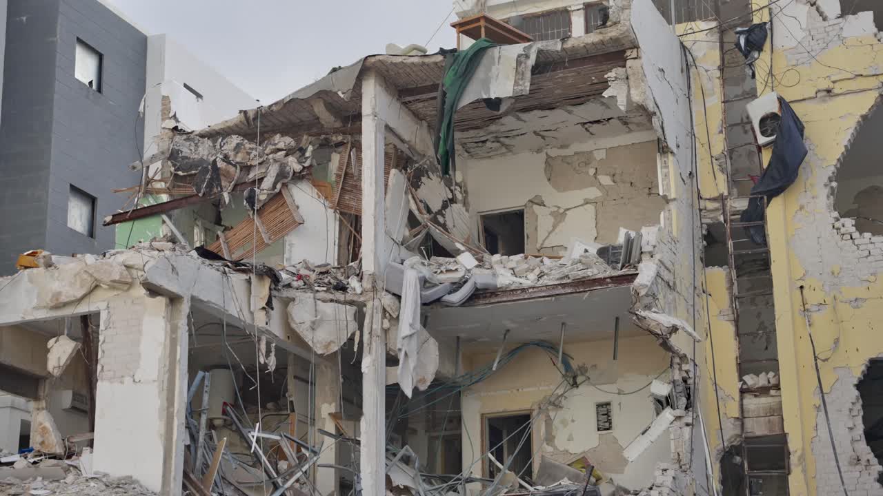 Collapsed apartment block.exposed rooms, shattered walls, twisted rebar and debris hanging from floors. conflict aftermath, missile airstrike damage, disaster response, humanitarian, reconstruction