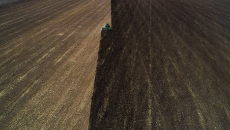 toma aérea de 4k de un dron que se desplaza hacia arriba para revelar un tractor disparándose a través de un campo