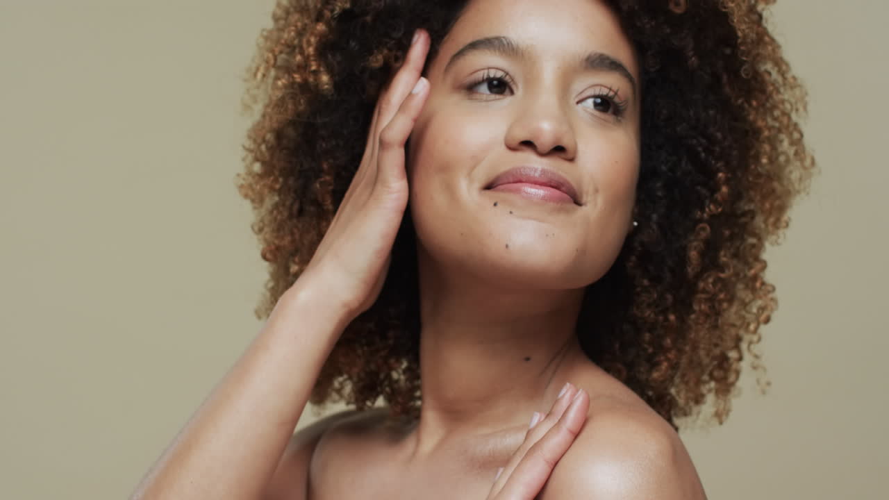 Mulher birracial feliz com cabelo cacheado escuro em fundo bege, em câmera lenta.