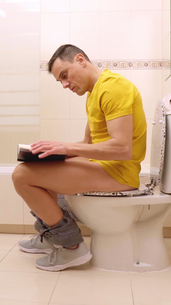 Man reading on toilet in bathroom
