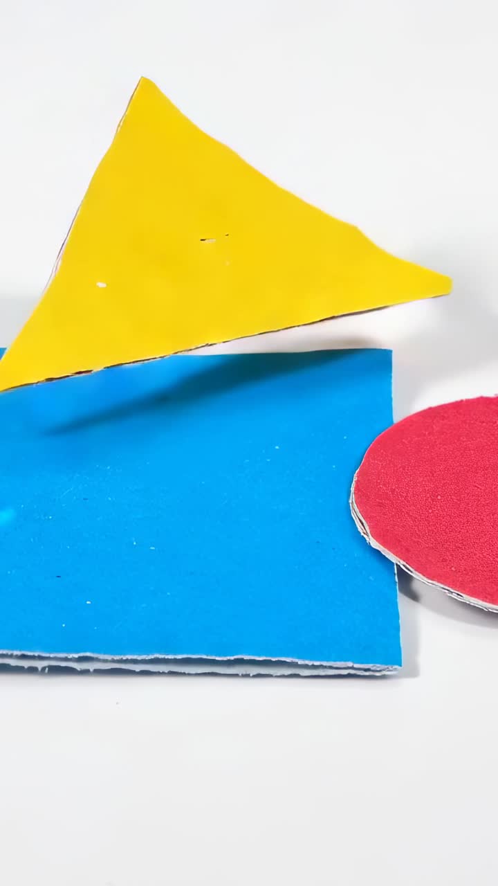 Video verticale: mano che spinge un triangolo giallo formando un tetto, poi esce da una base blu su una scrivania con un cerchio rosso