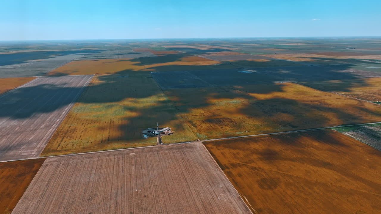 Vast landscape divided into the fields. Shadows from clouds move by the land. Drone footage approaching the site for oil business.