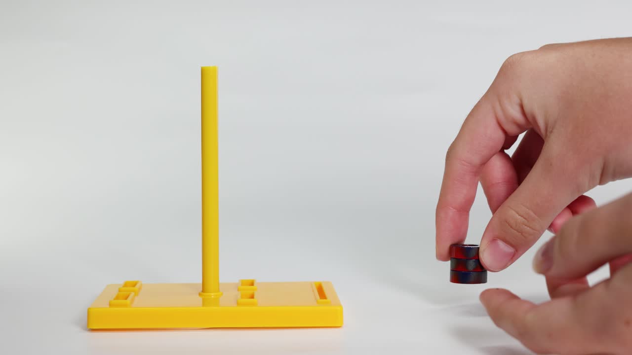 Hands manipulate magnets on a yellow stand, illustrating magnetic attraction and repulsion in a well-lit, static environment