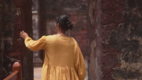 a woman in a yellow dress stands in a rustic, blurred background