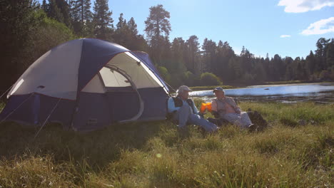 senior couple sitting outside tent drinking near a lake