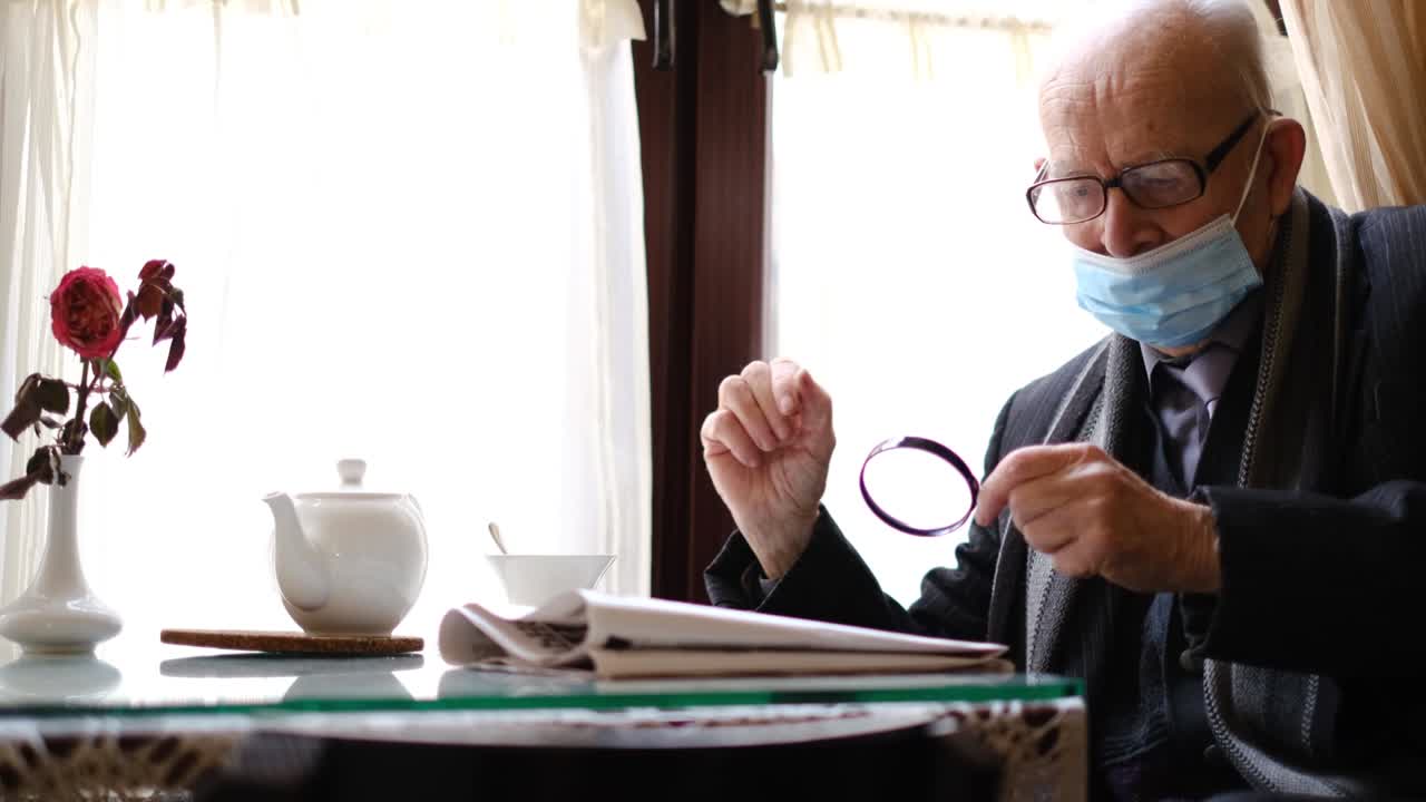 Gray-haired grandfather is sitting in a cafe drinking tea, he is reading a newspaper.