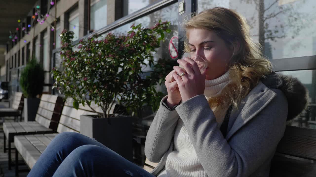 Kvinde puster på og nipper til en kop varm kaffe, siddende på en gadebænk om morgenen.