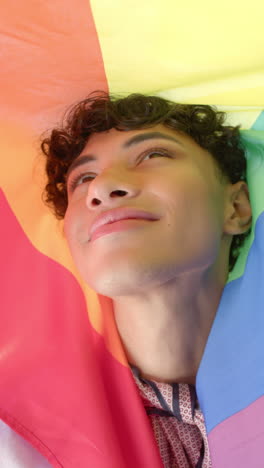 vertical video: smiling person wrapped in rainbow flag, embracing pride and joy at home