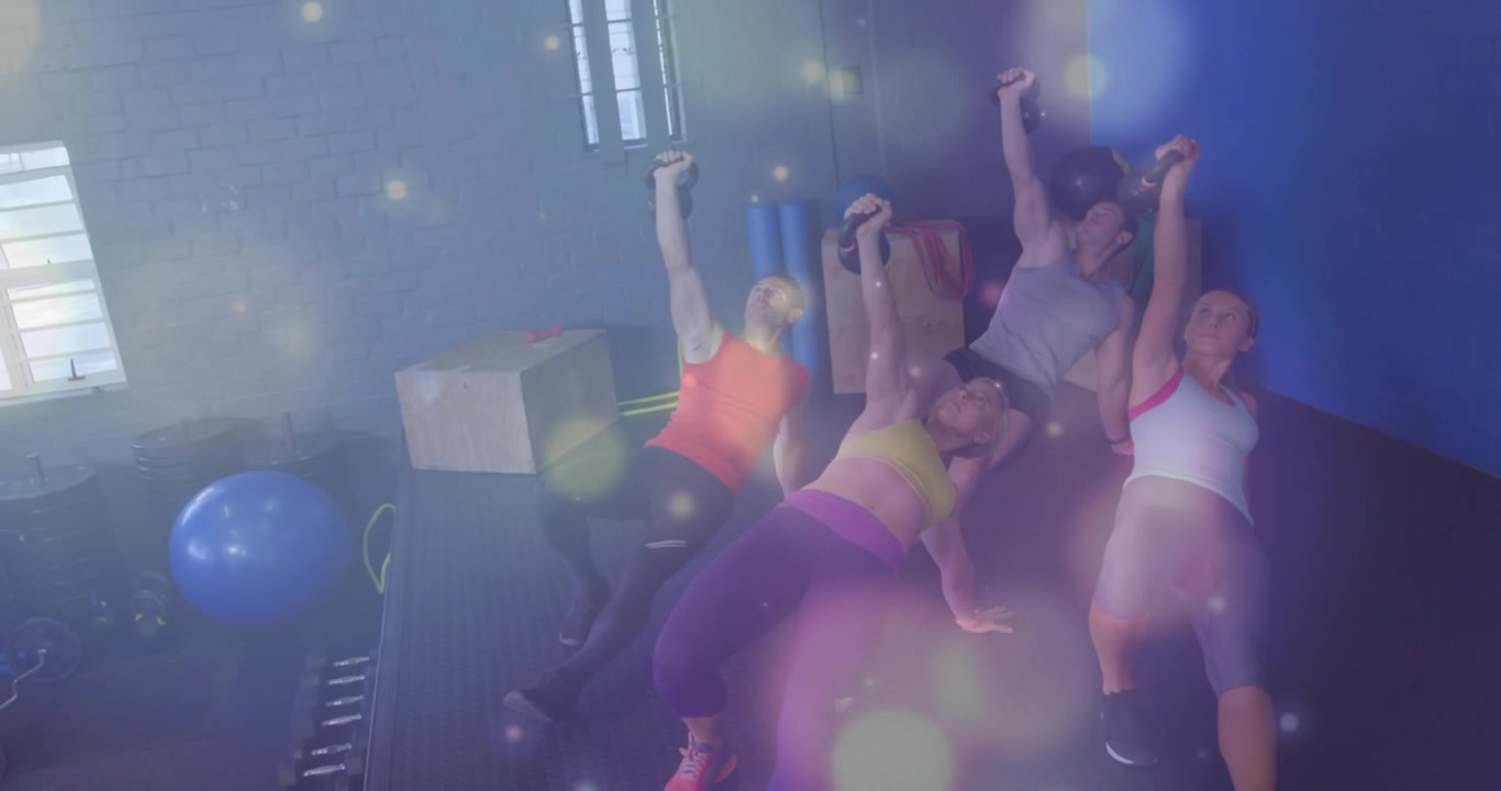 Fitnessgrupp börjar liggande på rygg, pressar vikter uppåt för styrka med bokeh-ljus som stiger över kropparna.