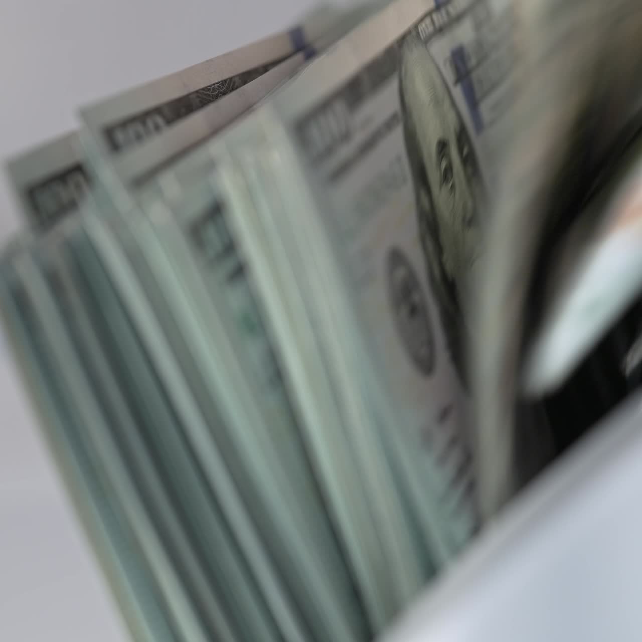 Hundred dollar bills falling on the holder in cash counting machine. Money counted machine stops working. Close up. Blurred backdrop