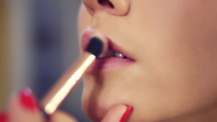 Professional makeup artist applying lipstick primer on lips of model working in beauty fashion industry. Close Up view of and