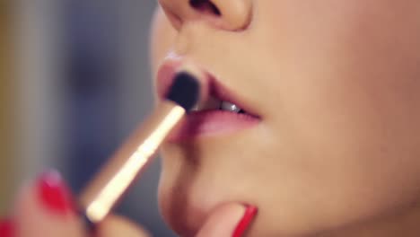 professional makeup artist applying lipstick primer on lips of model working in beauty fashion industry. close up view of and