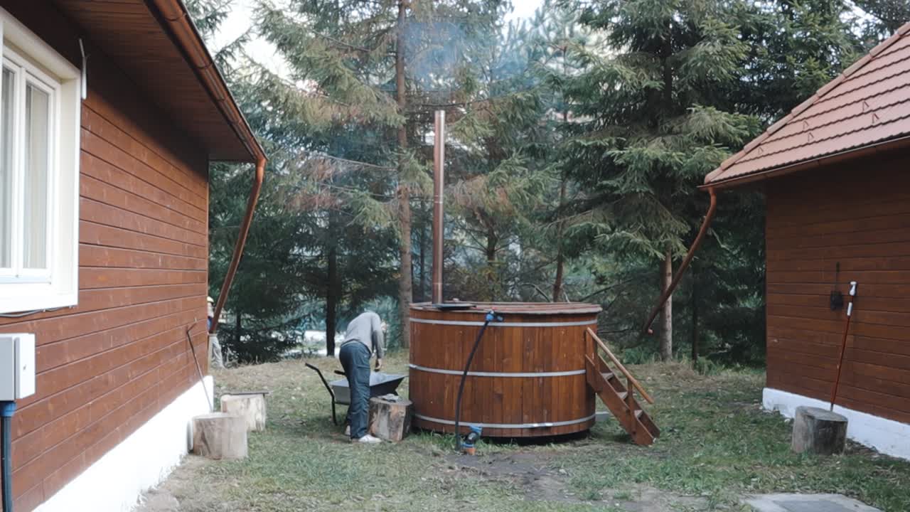 hombre poniendo madera en el horno de un jacuzzi de madera tradicional al aire libre