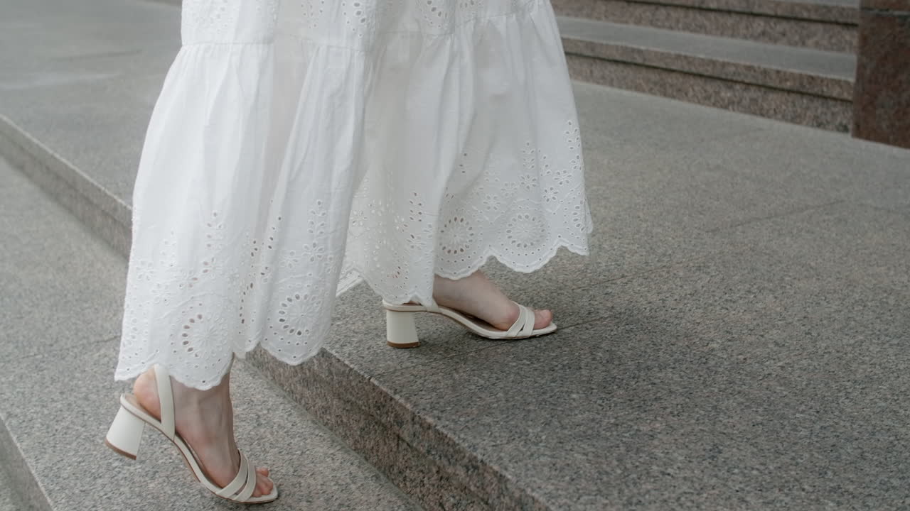 Woman walking up stairs in a white dress and white heels