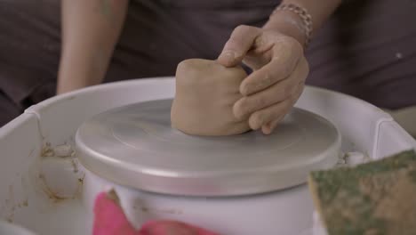 ceramic artist throws clay on potters wheel and spins to begin forming earthenware pot close-up