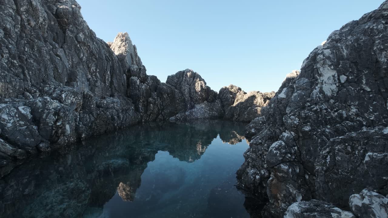 Increspatura in una piscina d'acqua limpida circondata da un'alta roccia.