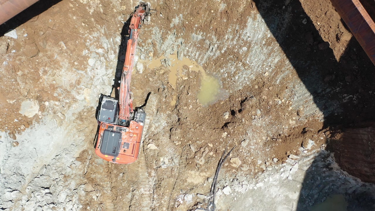Drone shot of excavator and ground improvement machine working under steel strut pipes in deep foundation excavation. Shoring systems in engineering and heavy industry.