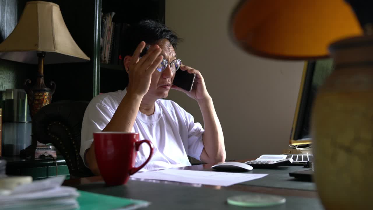 Asian Chinese businessman talking on the phone with hand gesture. Home setting. Work at home concept.