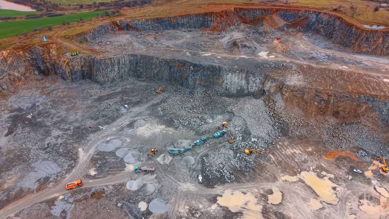 Aerial view of open pit granite quarry with mining equipment. Wide shot of a stone quarry with excavators, trucks, and processing machinery on a rocky ground