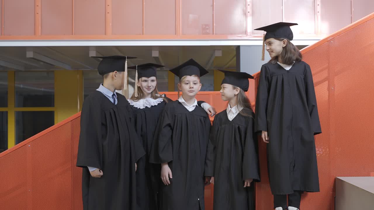 увеличение изображения счастливых воспитанников детского сада в шапочках и мантиях, смотрящих в камеру и делающих знак "большой палец вверх" во время церемонии вручения дипломов в детском саду