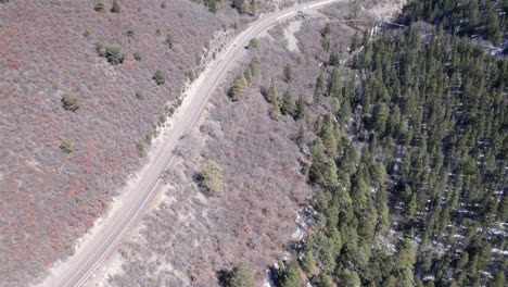 Top-down-view-of-a-rural-mountain-highway-flies-to-a-historic-truss-bridge-with-narrow-gauge-railway-near-Cloudroft,-New-Mexico