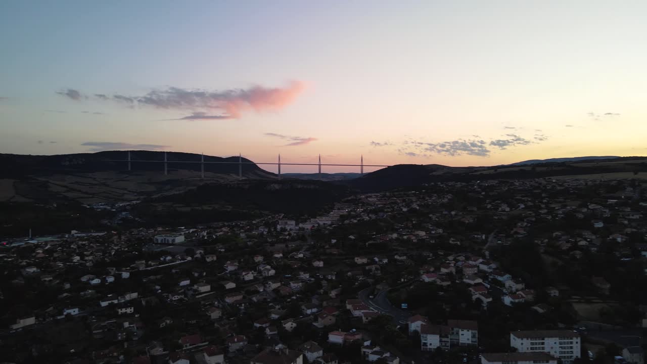 Aerial panoramic view of beautiful french city of Millau, France and famous Millau viaduct after sunset. Romantic french city nested among the hills in the evening golden hour light