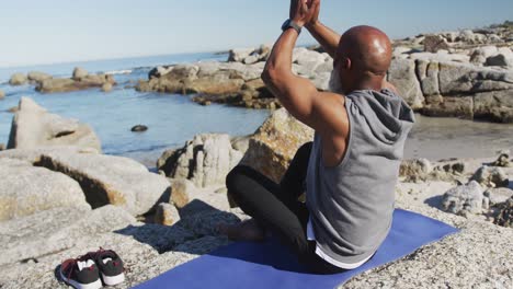 senior african american man exercising stretching on rocks by the sea