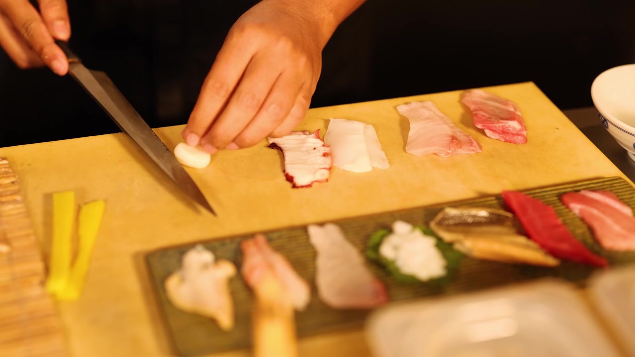 Primo piano delle mani dello chef che affettano pesce crudo e dispongono il sashimi su un tagliere di legno