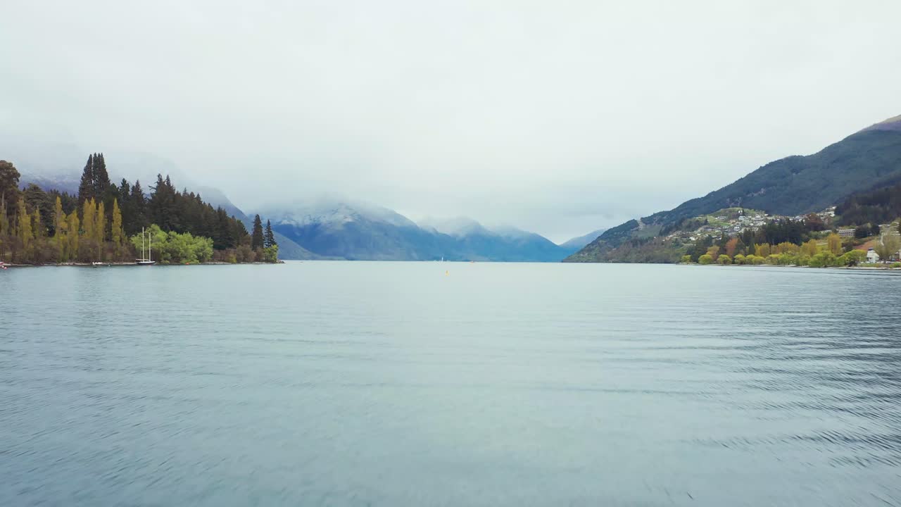 Vue aérienne au-dessus du lac Queenstown se dirigeant vers des montagnes enneigées par un temps maussade.