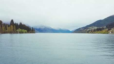 Aerial-shot-over-the-Queenstown-Lake-heading-towards-snow-topped-mountains-on-a-moody-day