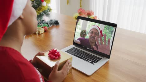 Afroamerikanische-Frau-Mit-Weihnachtsmütze-Nutzt-Laptop-Für-Weihnachtsvideoanruf-Mit-Mann-Auf-Dem-Bildschirm