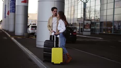 elegante, joven pareja con equipaje de pie en el estacionamiento del aeropuerto con sus maletas. esperando el coche después de la llegada