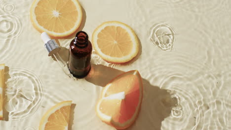 video de la botella del producto de belleza, pipeta, rebanadas de naranja en agua con espacio de copia en fondo amarillo