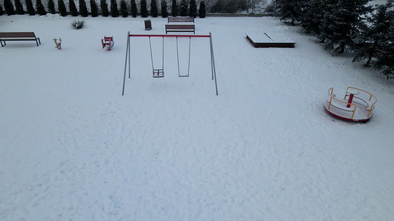 columpios y bancos vacíos en un parque infantil cubierto de nieve durante la temporada de invierno en lubawa, polonia