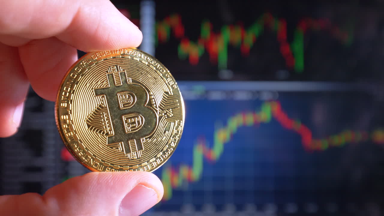 dedo masculino sosteniendo bitcoin dorado en luz y curvas de índice bursátil en segundo plano, cerrar