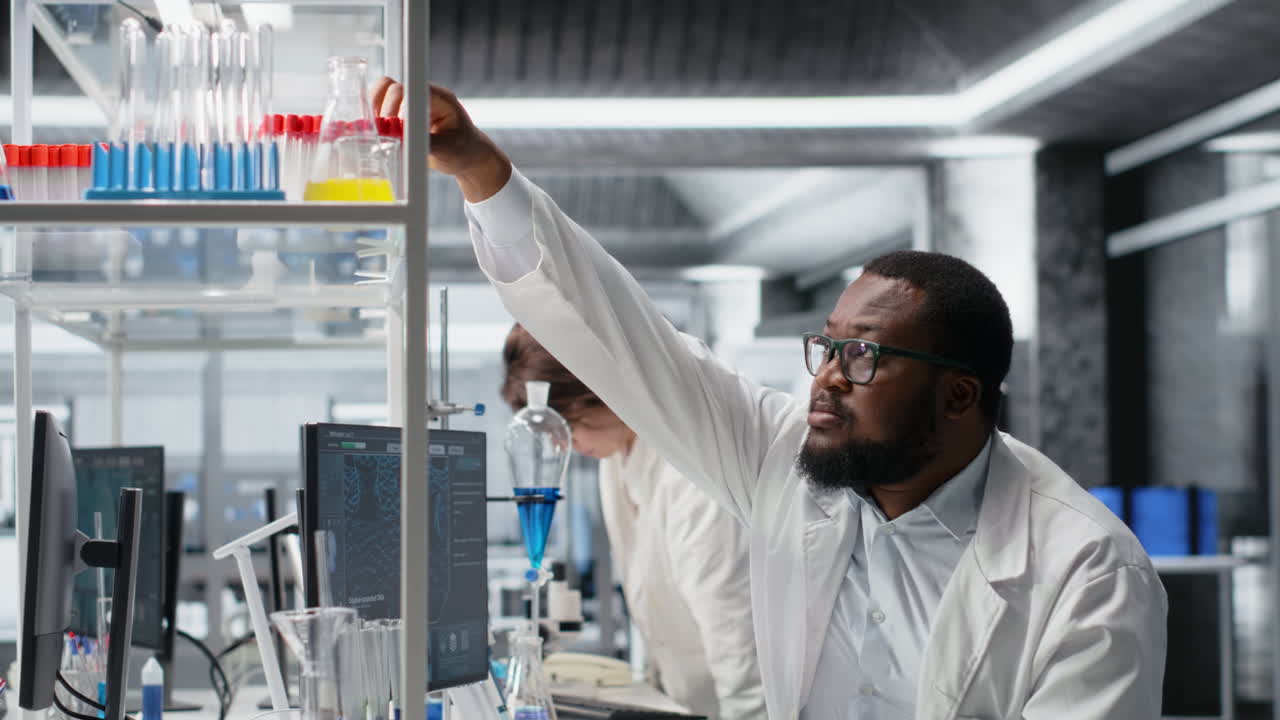 Vertical video Clinical microbiologist in lab looking at blood sample in test tube, using PC