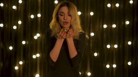 young beautiful woman blowing gold glitter confetti