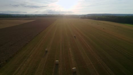 aerial drone forward moving shot of sunlight falling on golden field with hay bales or straw bales after harvest